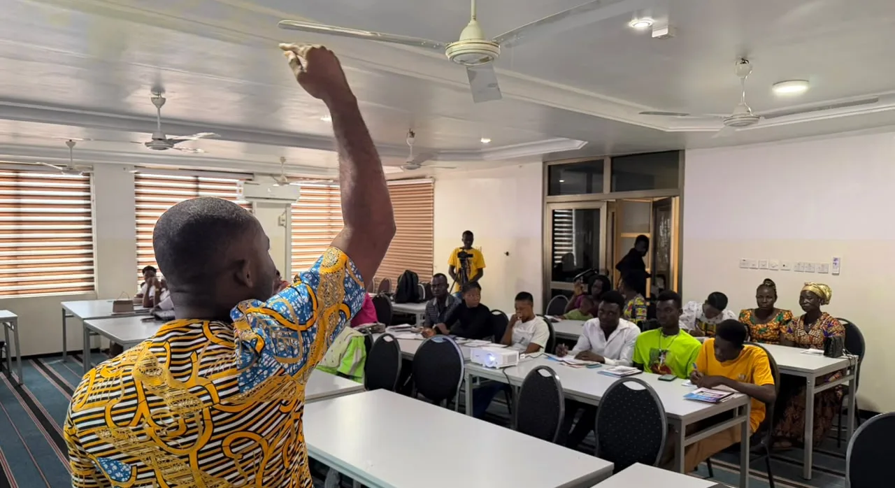A tutor with his arm raised teaching a room of seated students at GraceLife Institute