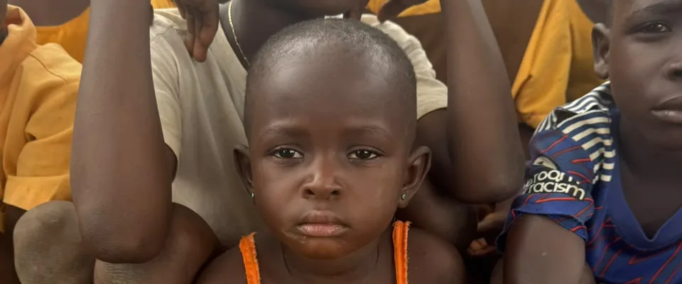 A young girl squatting among other children during a community outreach visit