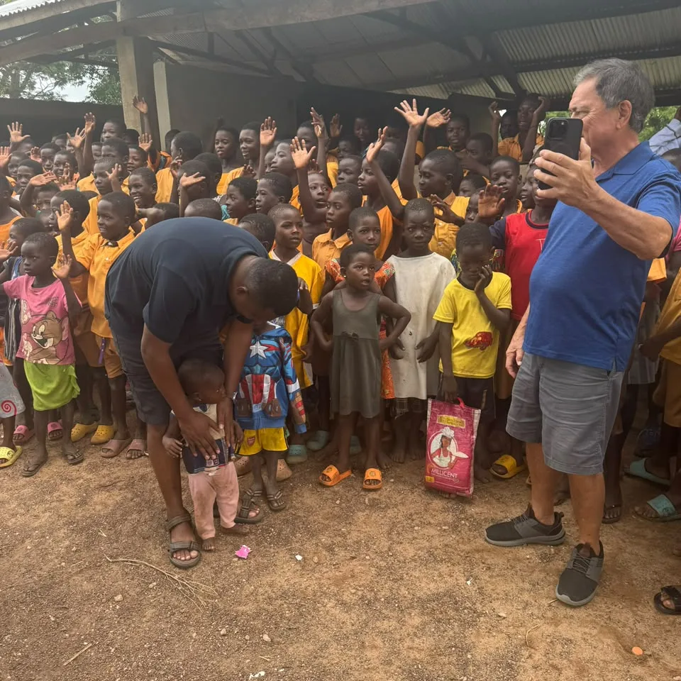 Schoolchildren waving and crowding round as visitors greet a toddler at a village school