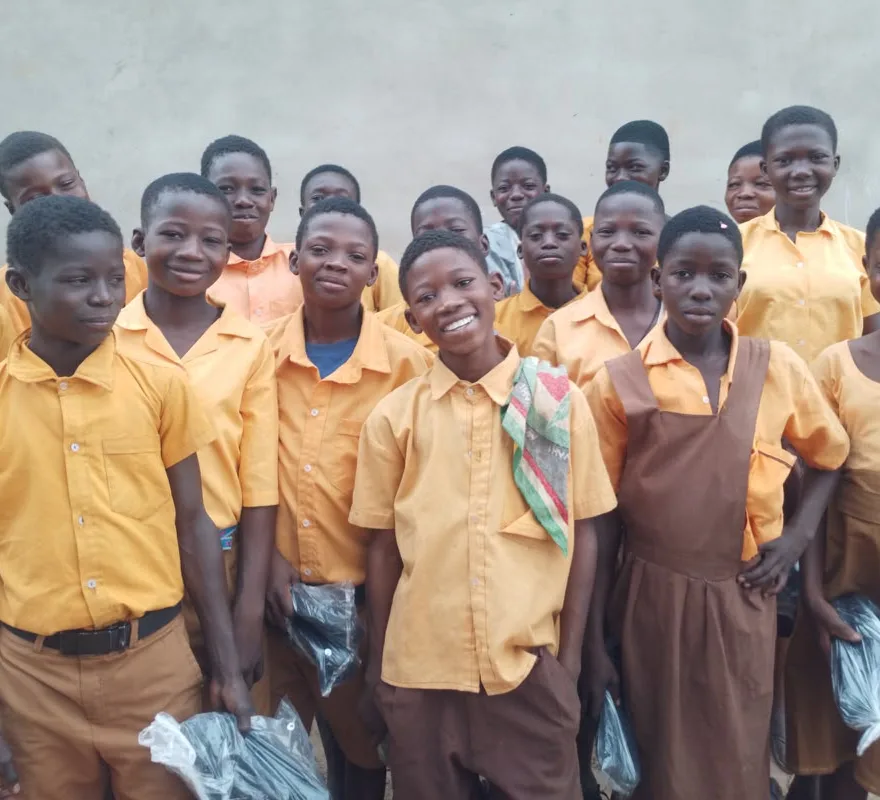 Schoolchildren in uniform smiling, holding packs of supplies handed out on an outreach